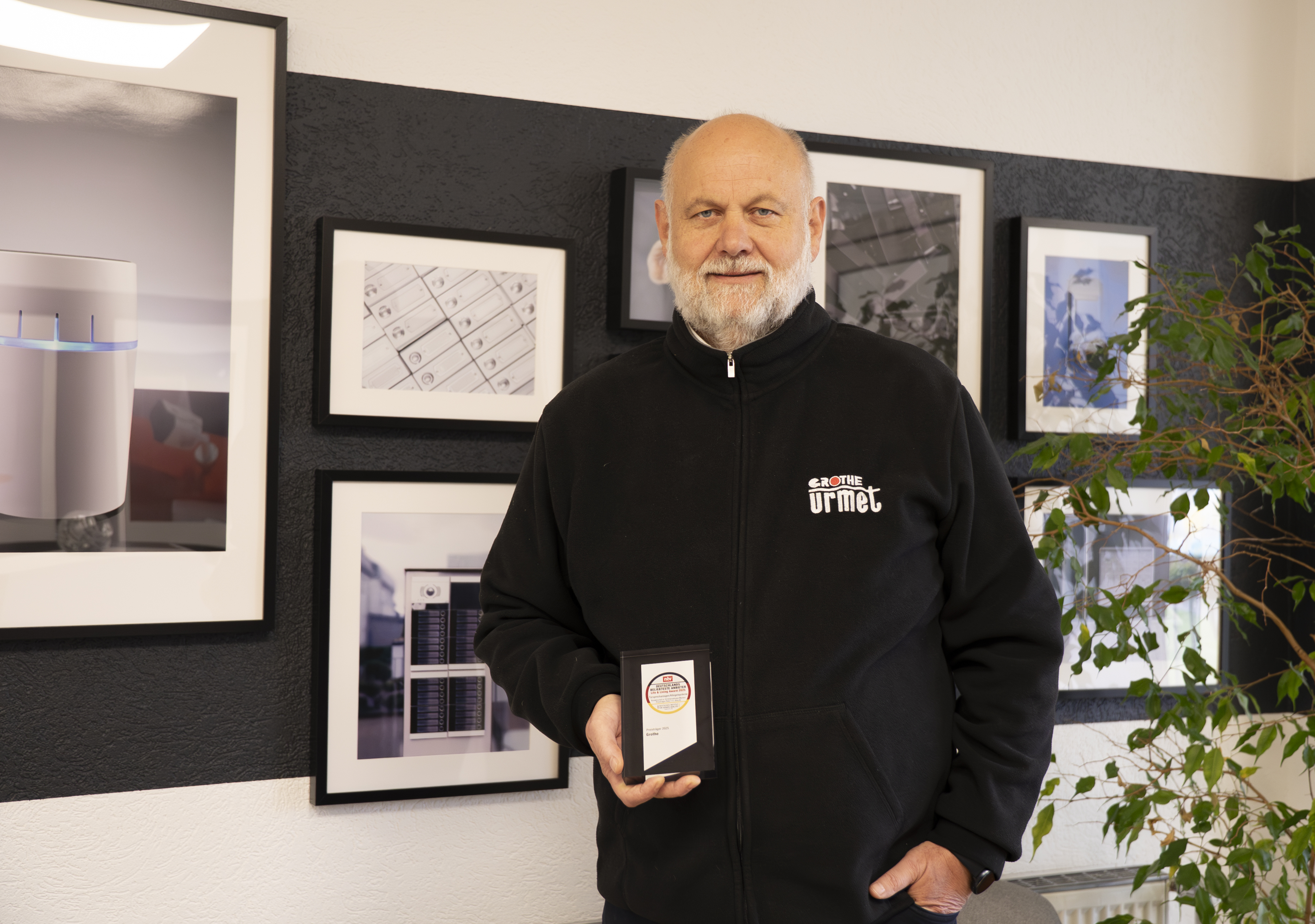 Geschäftsführer Andreas Rosen hält den Life & Living Award in einer Hand und blickt freundlich in die Kamera; im Hintergrund ist eine Bildergalerie zu sehen